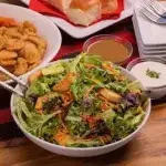 Family house salad featuring lettuce, tomatoes, cucumbers, and shredded carrots.